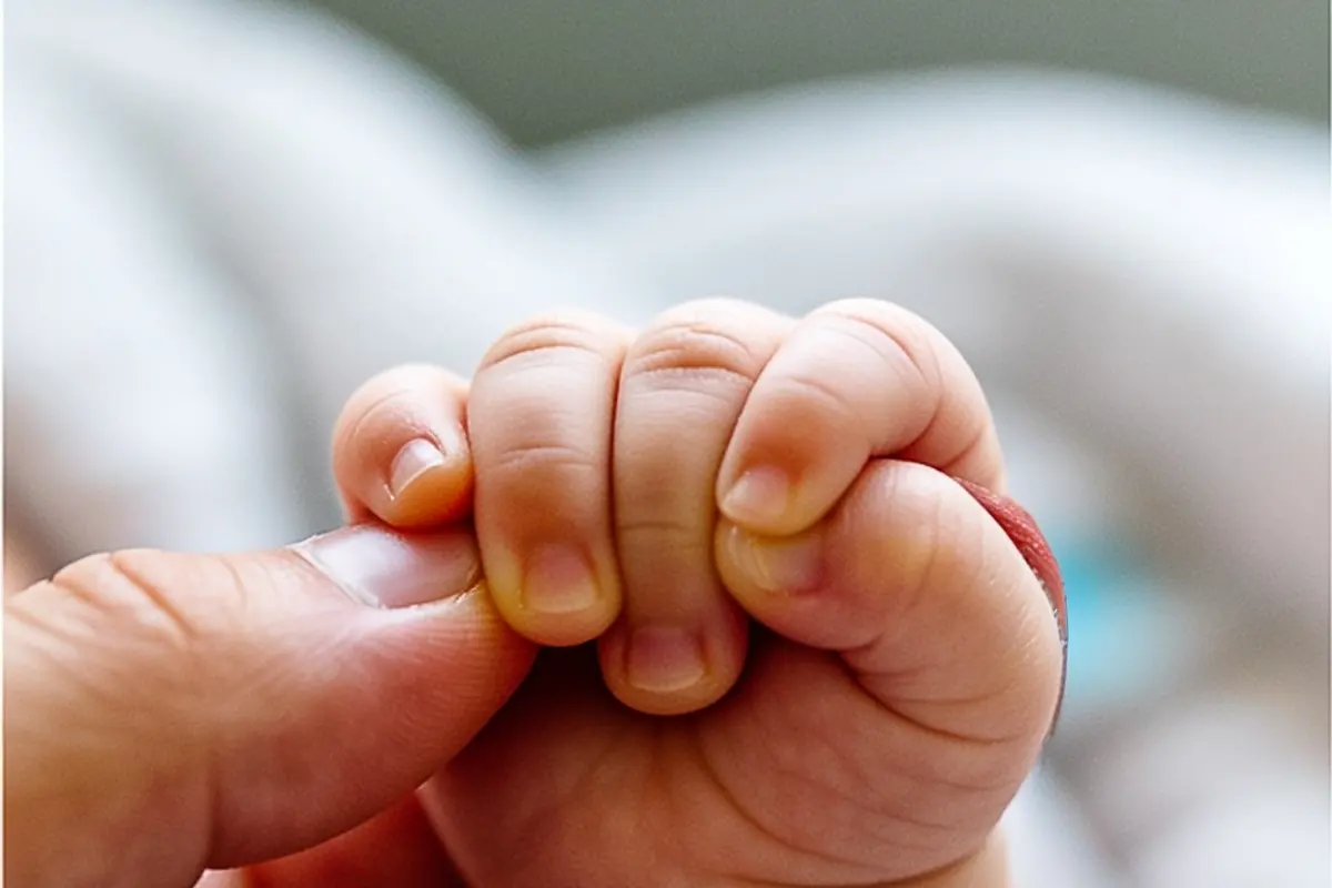 A newborn's tiny hand tightly grips an adult's finger.