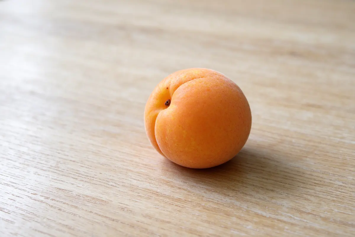 A single small apricot on a plain pale wooden table, soft window light.
