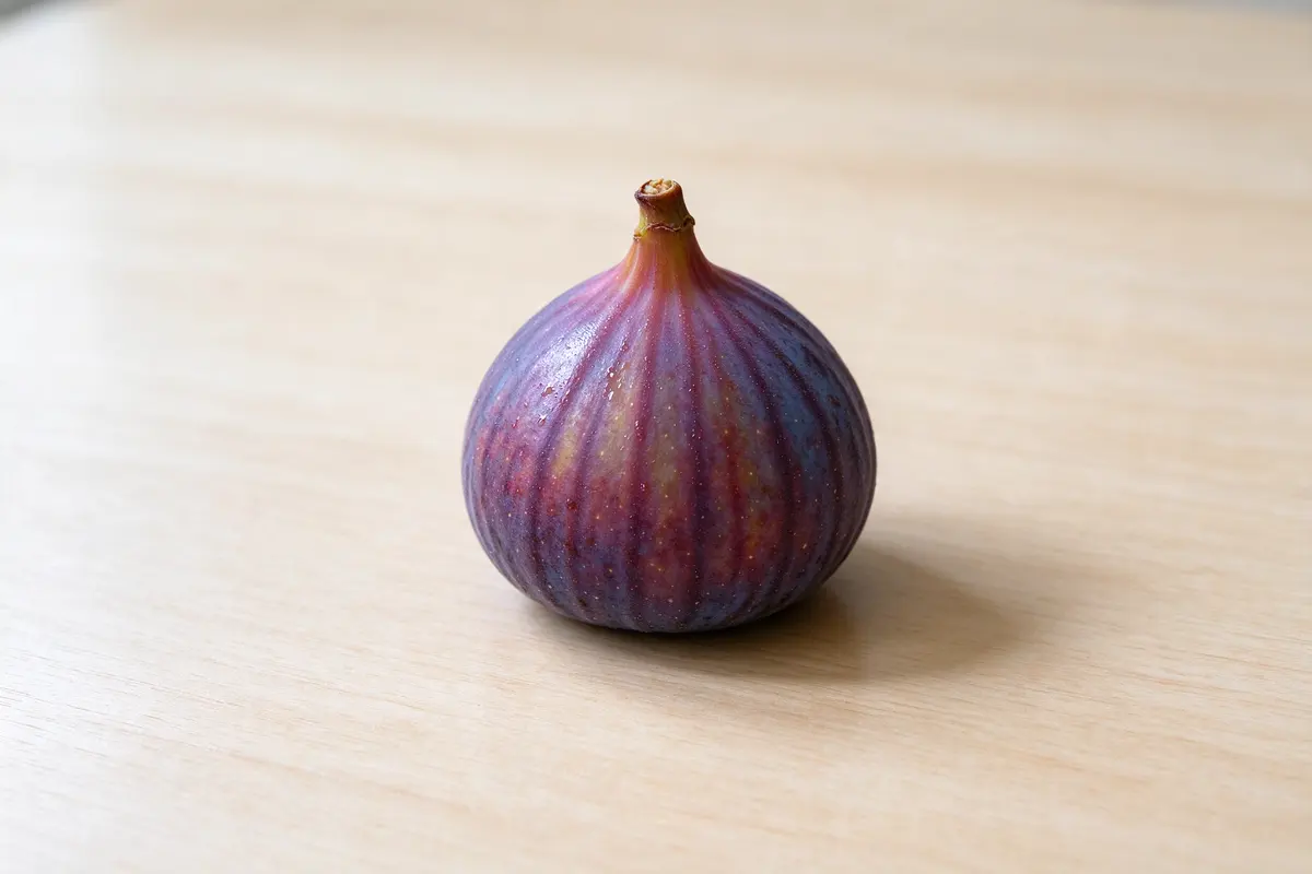A single purple fig on a plain pale wooden table, soft window light.